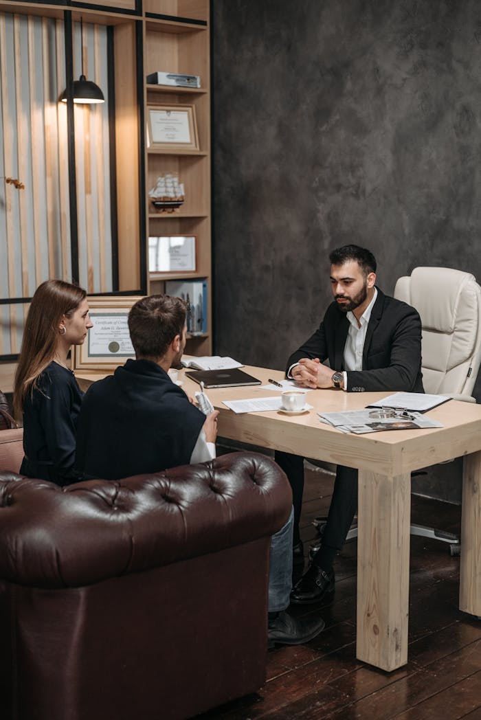A professional business meeting with three people discussing documents in an office setting.