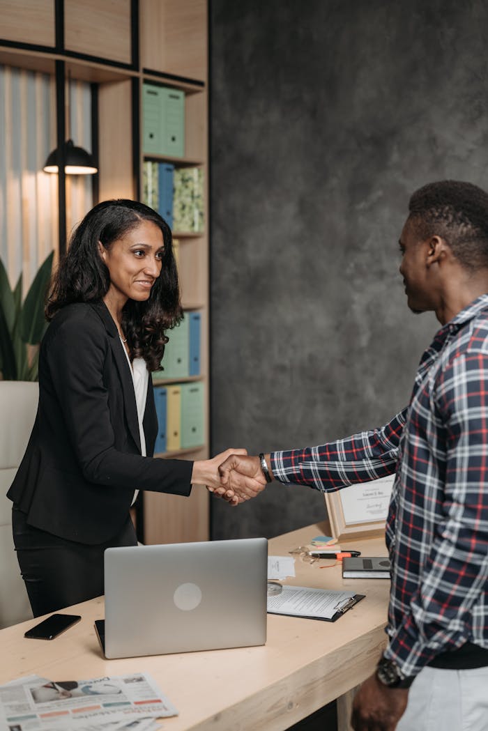 Two professionals shaking hands in an office setting, symbolizing a successful business partnership.